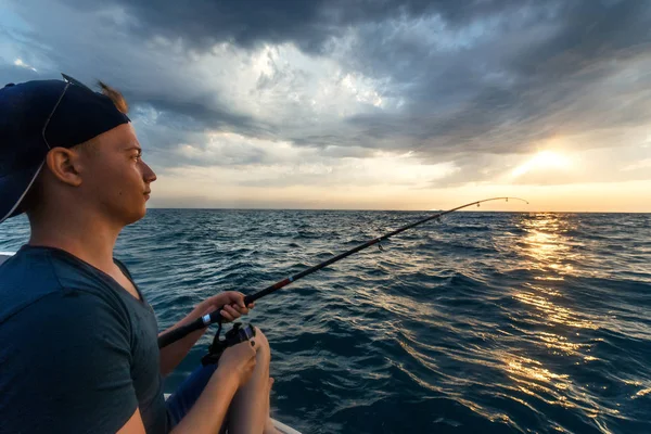 Młody człowiek połowów przez spinning w łodzi w otwarte morze. Seascape zachód słońca. — Zdjęcie stockowe