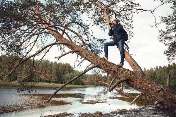 Männlicher Fotograf fotografiert einen schönen Fluss in der Taiga, der auf einer umgestürzten Kiefer steht — Stockfoto