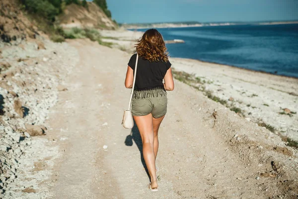 Vista trasera de hermosa hembra con piernas bronceadas perfectas en pantalones cortos que van en la costa en el campo . — Foto de Stock