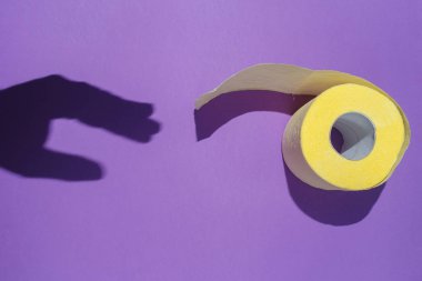 The hand shadow reaches for the yellow toilet paper on violet background. The concept of hygiene, issues of digestion. Flat lay, top view clipart
