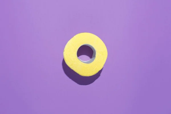 Жовтий рулон туалетного паперу на фіолетовому фоні. Плоска композиція — стокове фото