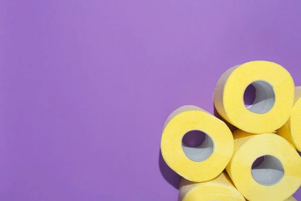 Минималистическая композиция с рисунком ярко-желтых рулонов туалетной бумаги на фиолетовом фоне. Плоская композиция, вид сверху — стоковое фото