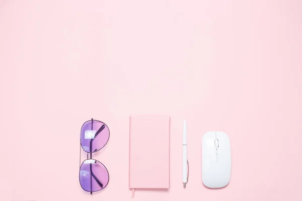 Pink colored desk with pink colored diary, white pen, white mouse and purple sunglasses. Minimalistic flat lay composition with copy space for bloggers, designers, magazines etc