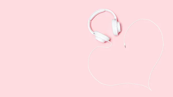 Headphones with a cord in the shape of a heart on pink background. Minimalistic flat lay composition with copy space for bloggers, designers, magazines etc