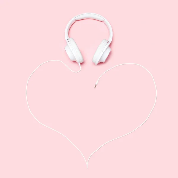 Auriculares con un cordón en forma de corazón sobre fondo rosa. Composición plana minimalista con espacio de copia para blogueros, diseñadores, revistas, etc. — Foto de Stock