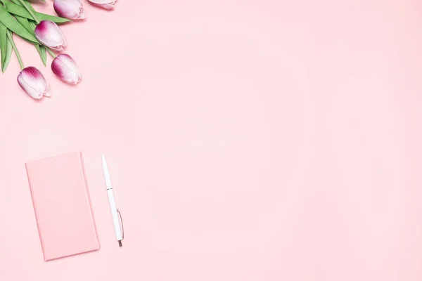 Escritorio de color rosa con tulipanes púrpura, diario rosa, pluma blanca. Composición plana minimalista con espacio de copia para blogueros, diseñadores, revistas, etc. — Foto de Stock
