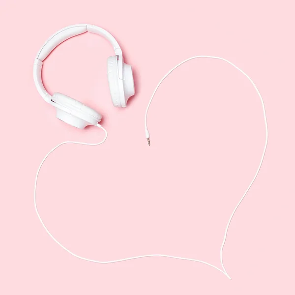 Headphones with a cord in the shape of a heart on pink background. Minimalistic flat lay composition with copy space for bloggers, designers, magazines etc