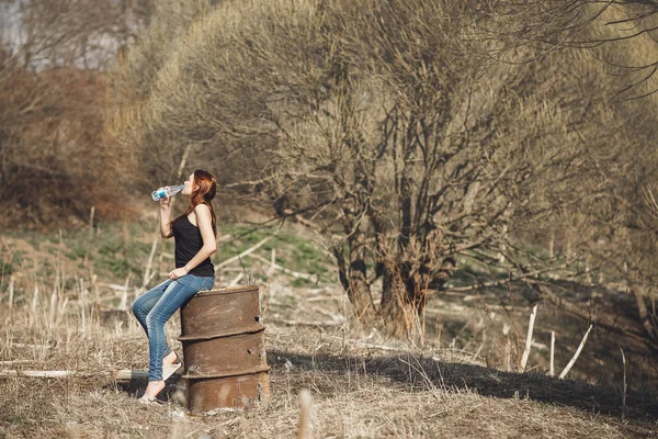 在公园阳光明媚的春日, 年轻女子从瓶子里喝冷水. — 图库照片