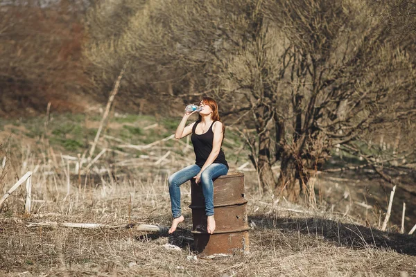 在公园阳光明媚的春日, 年轻女子从瓶子里喝冷水. — 图库照片
