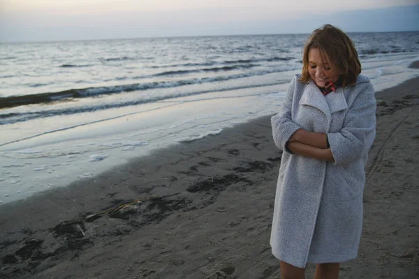 Šťastná dívka chodí v kabátě podél pobřeží večer — Stock fotografie