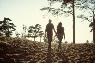 Tatil çift birlikte birbirleri etrafında tutarak aşık Sahilde yürüyüş. Arkadan Görünüm. Çam ağaçları ile sahilde sıcak gün batımı. Balayı konsepti