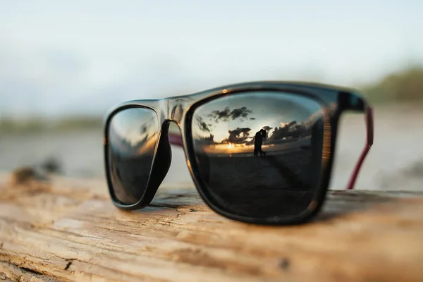 Солнечные очки и обнимающая пара в отражении от очков — стоковое фото