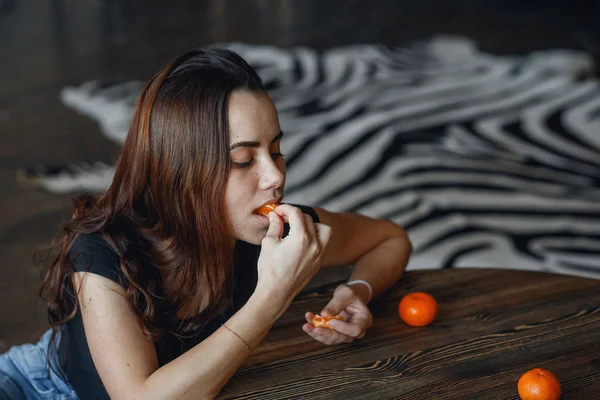 Młoda dziewczyna jedzenia słodkich mandarynki, siedząc na podłodze w pobliżu tabeli — Zdjęcie stockowe