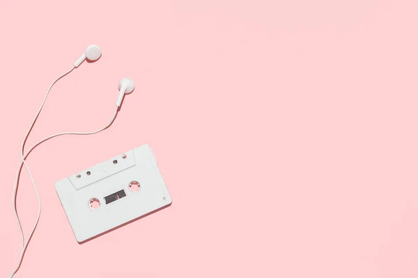 Cinta de casete blanca y auriculares sobre fondo rosa —  Fotos de Stock