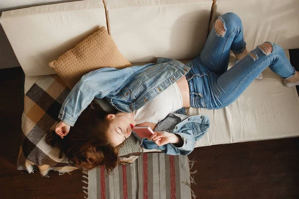 Mulher jovem bonito em jeans roupas deitado no sofá com diário rosa — Fotografia de Stock