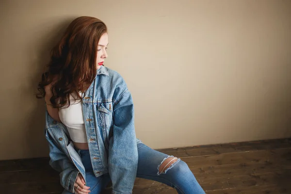 Sensuele vrouwelijke model poseren in denim jasje, jeans en witte sokken op de vloer in de buurt van beige muur. Terug naar de jaren negentig fashion lifestyle stijl concept — Stockfoto