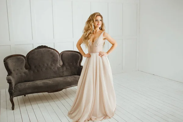 Krásná blondýnka s řeckým účesu v béžových prášků svatební šaty pózové ve studiovém sále — Stock fotografie
