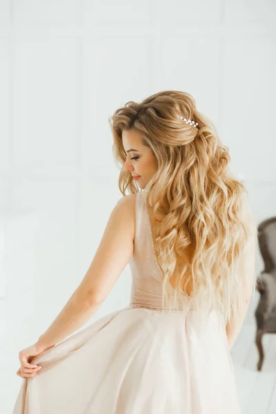 Schöne blonde Frau mit griechischer Frisur in beige pudrigem Atlas-Hochzeitskleid posiert im Studiozimmer — Stockfoto
