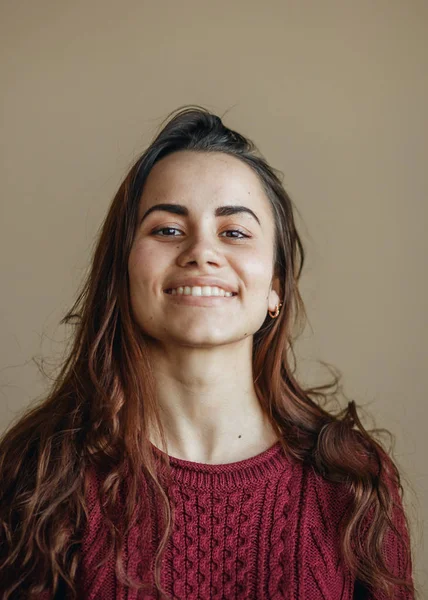 Mujer joven feliz mirando a la cámara en la pared de color beige. Ella se vistió con suéter de color burdeos —  Fotos de Stock