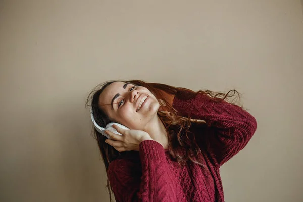 Nikmati musiknya. Wanita muda bahagia menyenangkan musik di headphone putih. Dia mengenakan sweater burgundy — Stok Foto