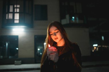 Gece şehrinde yanan çakmağı olan genç kızıl saçlı kadın.