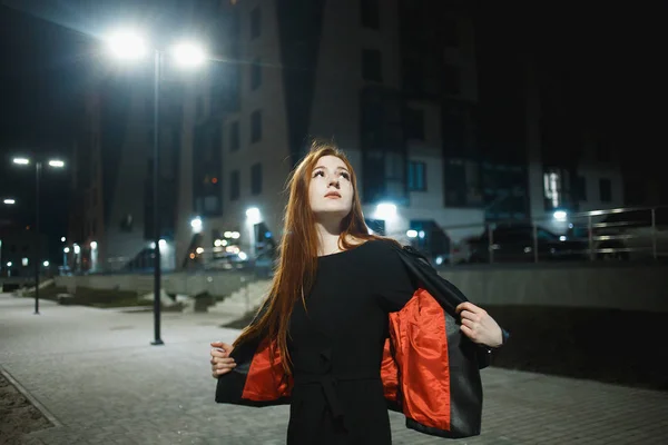Таинственная рыжая женщина в элегантной кожаной куртке и на высоких каблуках ходит по городской улице, нуар атмосфера, интригующая концепция — стоковое фото