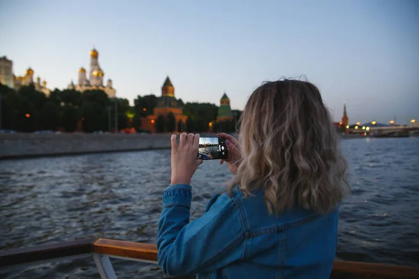 Woman tourist taking pictures on mobile phone during the boat trip on the Moscow river on the background the Kremlin. Travel to Russia concept
