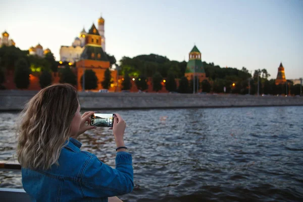 Woman tourist taking pictures on mobile phone during the boat trip on the Moscow river on the background the Kremlin. Travel to Russia concept
