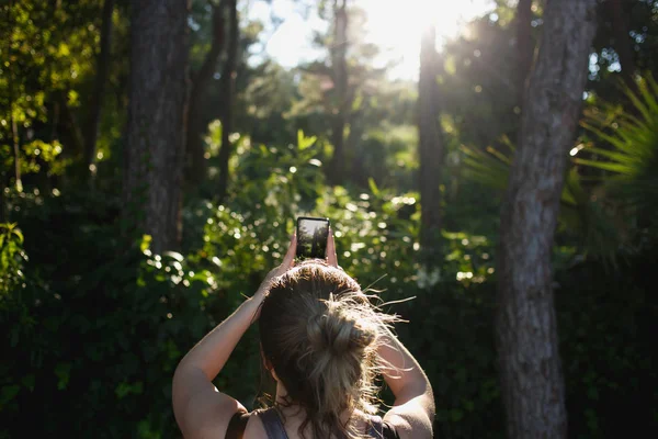 Woman taking pictures of tropical forest in backlight — Stock Photo, Image