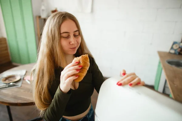 Pretty smiling ginger girl eating croissant in the morning kitchen — Stock Photo, Image