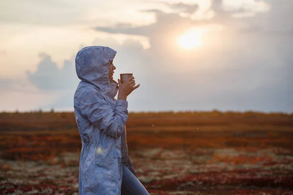 旅行女孩喝茶从热水瓶，户外。年轻女子在杯子里喝酒。主题旅行。秋天的日落冻土带 — 图库照片