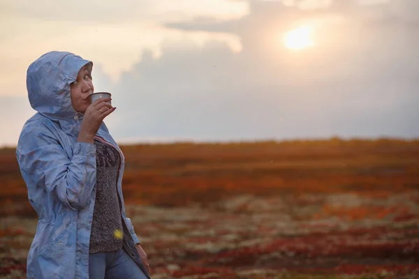 Reiseleiterin trinkt Tee aus Thermoskanne, draußen. junge Frau trinkt bei Tasse. Themenreisen. Sonnenuntergang in der herbstlichen Tundra — Stockfoto