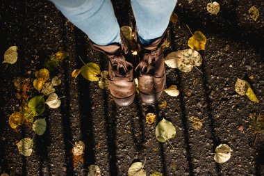 Sonbaharda botlar sonbaharda dışarı çıkar. Kahverengi deri çizmeli ve bağcıklı güzel kadın ayakları mevsim, ayakkabı, insan ve doğa konsepti için sonbahar yapraklarını giyer. Güneşli bir hava. Üst görünüm kopyası