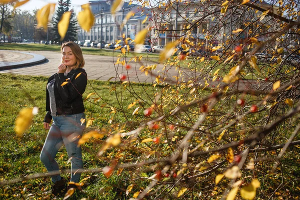Szczęśliwa młoda, zakrzywiona kobieta spoglądająca jesienią na zewnątrz. Dziewczyna ciesząca się ciepłą pogodą. Ma na sobie niebieskie dżinsy i czarną kurtkę. — Zdjęcie stockowe