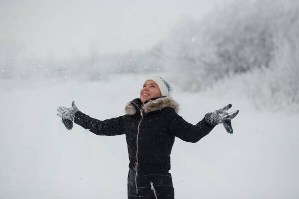 Winter fun, holidays, good weather and people concept - young woman blowing snow from mittens in snowy winter day