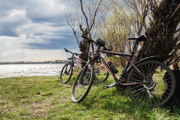 Two mountain bikes stand on the river bank. Atmospheric dynamic light. Picnic — Stock Image Two mountain bikes stand on the river bank. Atmospheric dynamic light. Picnic Royalty Free Stock Images