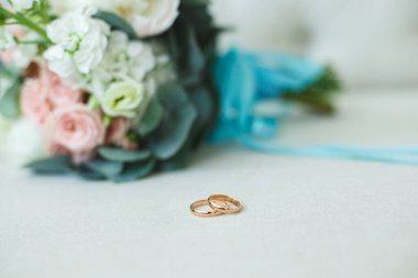 Beyaz güllerin düğün buketi, pembe güller ve hafif koltukta altın alyanslı şakayık.