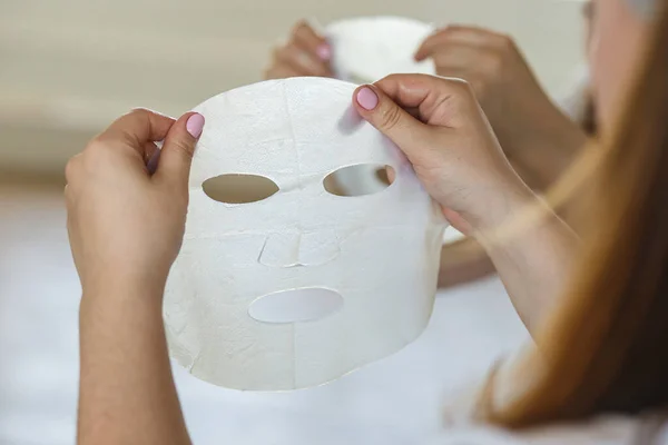 Zbliżenie na kobieta trzyma biały prześcieradło twarzy maska w łazienka w domu — Zdjęcie stockowe