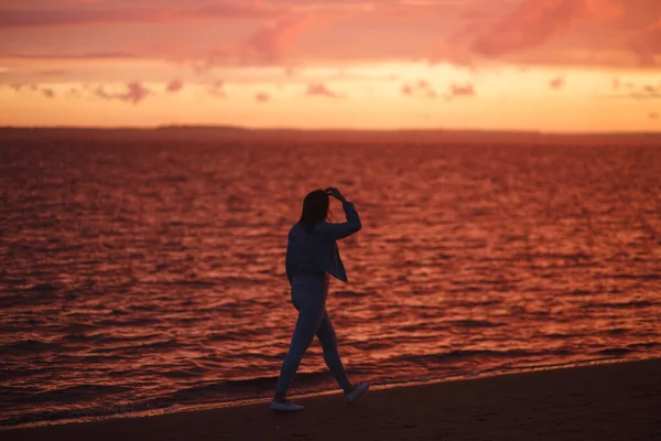 Frau spaziert allein am Strand und blickt nach dem Regen auf den bunten Sonnenuntergang. — Stockfoto