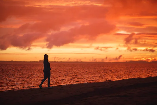 Frau spaziert allein am Strand und blickt nach dem Regen auf den bunten Sonnenuntergang. — Stockfoto