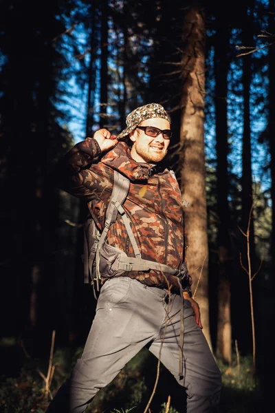 Hiker hiking in autumn forest. Male hiker in camouflage jacket with backpack looking to the side walking in forest. Caucasian handsome male outdoors in nature. Concept of forest wear, navigation