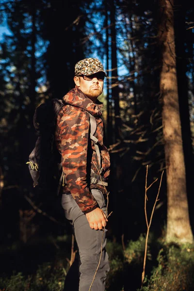 Wandern im herbstlichen Wald. Männlicher Wanderer in Camouflage-Jacke mit Rucksack, der zur Seite schaut, wenn er im Wald spaziert. Kaukasische stattliche Männchen im Freien in der Natur. Konzept des Waldverschleißes, Navigation — Stockfoto