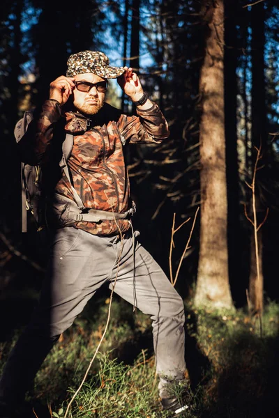 Wędrówki piesze w jesiennym lesie. Mężczyzna wędrowiec w kamizelce kamuflażowej z plecakiem wychodzącym na bok spacerujący po lesie. Biały, przystojny mężczyzna na świeżym powietrzu w naturze. Pojęcie zużycia lasów, nawigacja — Zdjęcie stockowe