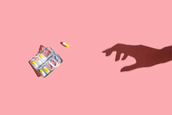 Tabletki w pęcherzu i cień dłoni na różowym tle. Płaskie ułożenie, widok z góry — Zdjęcie stockowe