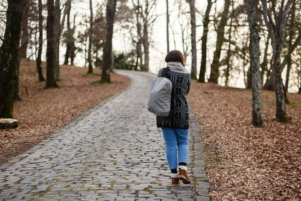Widok z tyłu kobieta z plecakiem spacery wzdłuż kamiennej drogi w jesiennym lesie — Zdjęcie stockowe