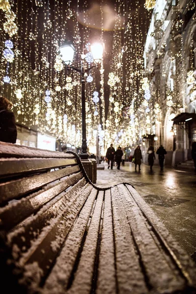 Lavička pokrytá sněhem na městské ulici ve slavnostním osvětlení — Stock fotografie