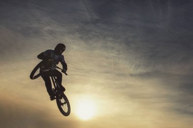 Güneşli gökyüzünde akrobatik atlayış yapan şehir motorcusu güneşli bir öğleden sonra ekstrem spor yarışmasında BMX bisikleti süren adam. Sıcak tonlu resim