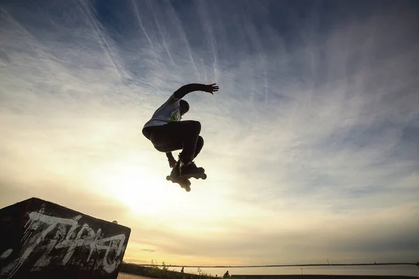 Onherkenbare roller op de extreme rolschaatsen die acrobatische sprong maken aan de zonnige hemel - Guy bij extreme sportcompetitie op zonnige middag - Alternatief lifestyle concept op warme zonneschijn kleuren — Stockfoto