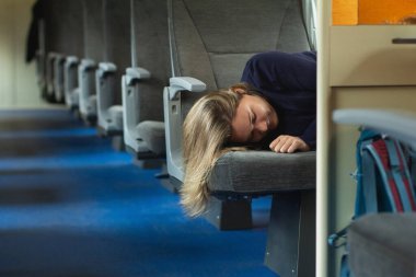 Banliyö treninde uyuyan genç bir kadın gezgin. Arka planda boş tren koltukları
