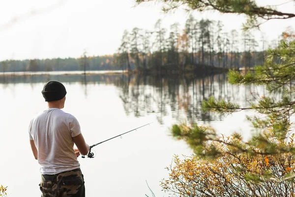 Pescador Pesca en spinning en hermoso lago de otoño por la mañana con bancos de conifeur bosque — Foto de Stock